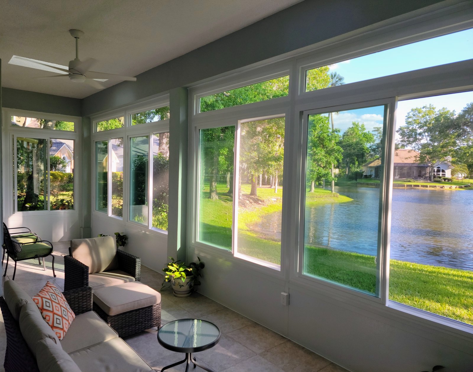 Interior of a sunroom with white-framed windows and transoms overlooking a lawn and pond, completed by Better Home Improvement in Jacksonville, FL